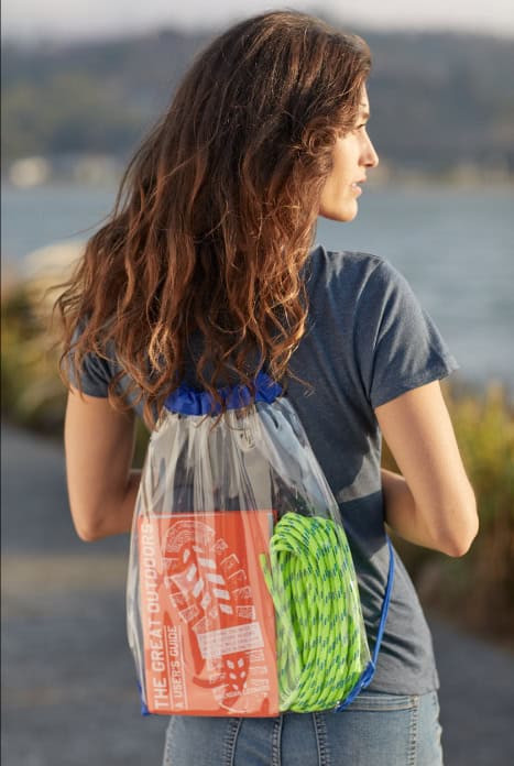 woman standing from behind wearing a clear drawstring backpack filled with a notebook and climbing rope